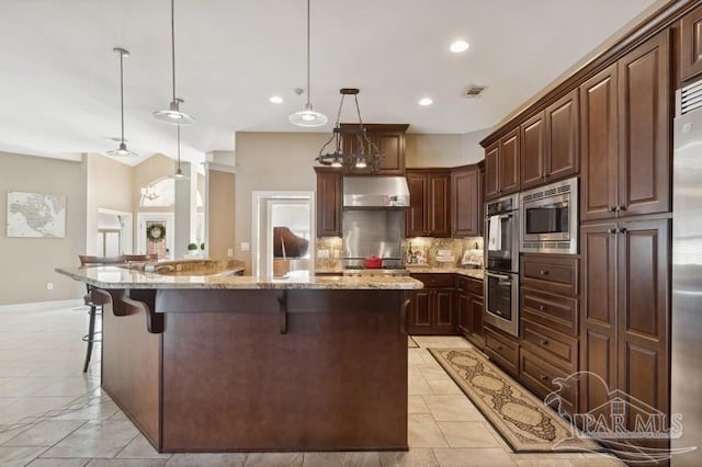 kitchen featuring tasteful backsplash, appliances with stainless steel finishes, light stone counters, and wall chimney exhaust hood