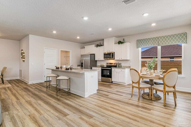 kitchen with a breakfast bar, appliances with stainless steel finishes, white cabinetry, light hardwood / wood-style floors, and an island with sink