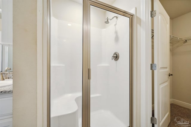 full bathroom featuring a stall shower, a walk in closet, and vanity