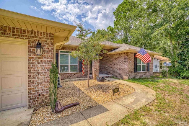 property entrance featuring brick siding, an attached garage, and roof with shingles