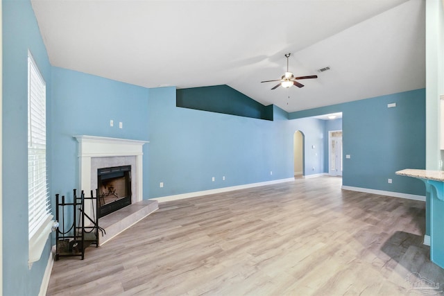 living room featuring light wood-type flooring, a tiled fireplace, arched walkways, and a ceiling fan