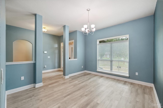 empty room featuring baseboards, an inviting chandelier, and light wood-style floors