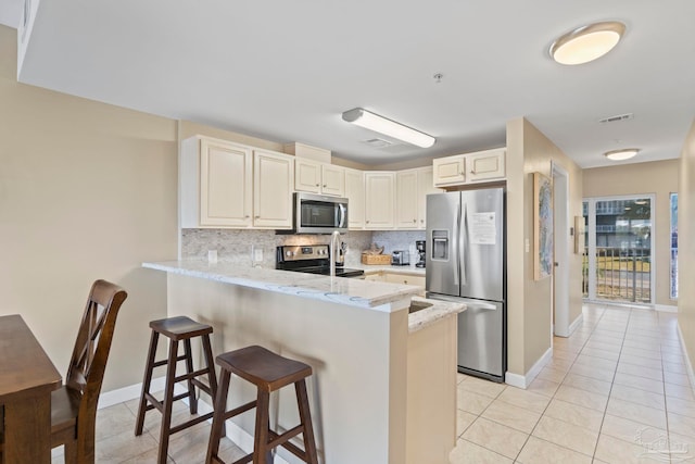 kitchen with appliances with stainless steel finishes, decorative backsplash, kitchen peninsula, a breakfast bar, and light tile patterned floors