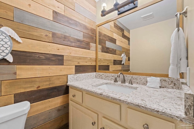 bathroom with toilet, vanity, and wooden walls