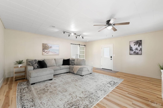 living area featuring a ceiling fan, wood finished floors, visible vents, and a barn door