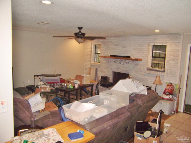 tiled living room featuring ceiling fan, brick wall, a fireplace, and a textured ceiling