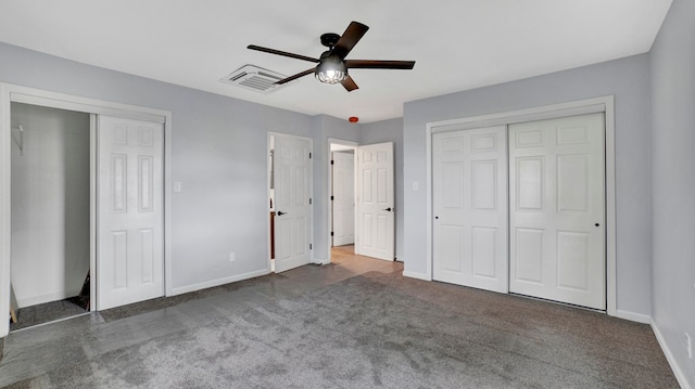 unfurnished bedroom featuring ceiling fan, two closets, and dark colored carpet