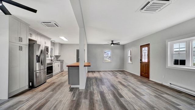 kitchen with stainless steel fridge, stove, white cabinetry, and butcher block counters