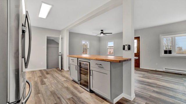 kitchen with wood counters, wine cooler, ceiling fan, stainless steel fridge, and baseboard heating