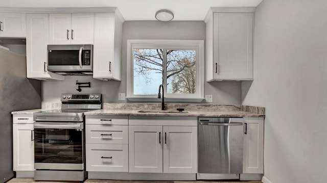 kitchen with white cabinets, sink, light stone countertops, and stainless steel appliances