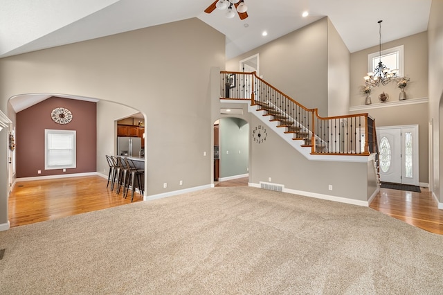 unfurnished living room with light carpet, ceiling fan with notable chandelier, and high vaulted ceiling