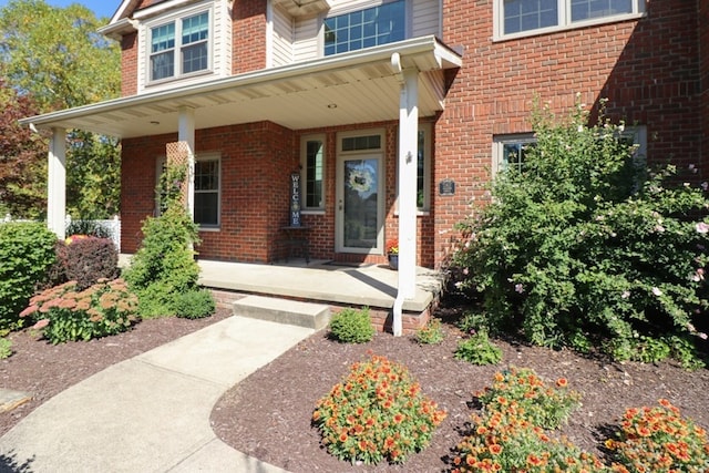 entrance to property with a porch and brick siding