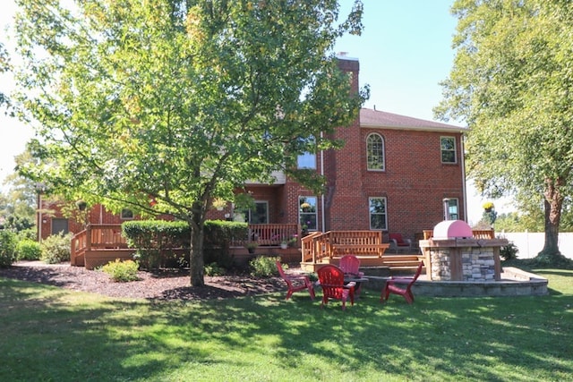 rear view of house featuring brick siding, a lawn, a chimney, and a wooden deck