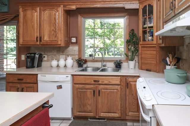 kitchen with brown cabinets, light countertops, white dishwasher, a sink, and under cabinet range hood