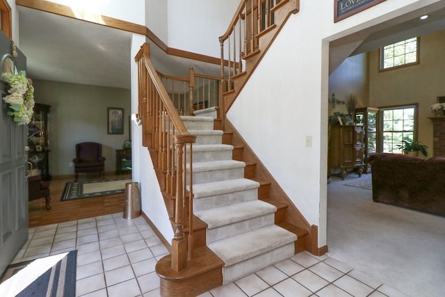 stairs featuring arched walkways, baseboards, tile patterned floors, carpet, and a high ceiling