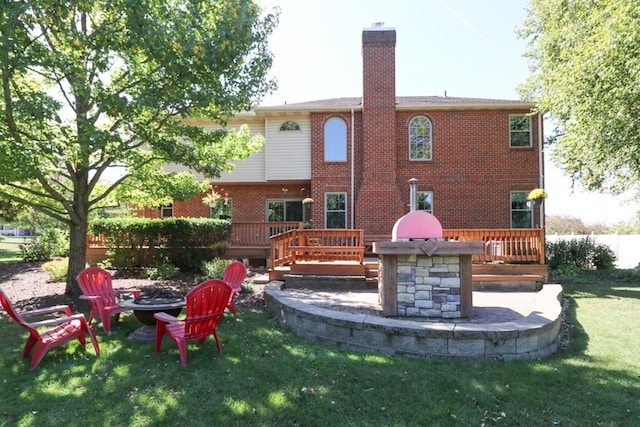 rear view of house with a fire pit, a lawn, a chimney, a deck, and brick siding