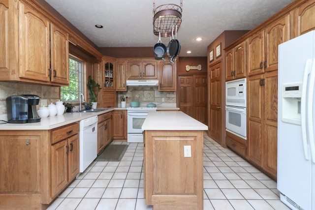 kitchen featuring light tile patterned floors, a kitchen island, a sink, white appliances, and under cabinet range hood