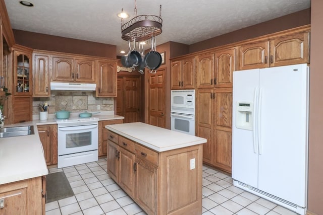 kitchen with backsplash, a kitchen island, a sink, white appliances, and under cabinet range hood