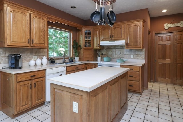 kitchen featuring white dishwasher, under cabinet range hood, stove, a sink, and brown cabinetry