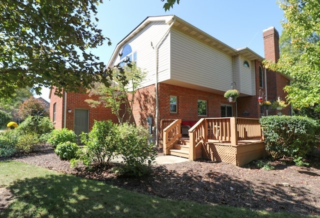 back of property featuring a deck, brick siding, and a chimney