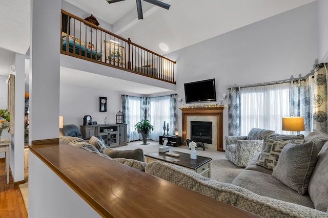 living area featuring light wood finished floors, a fireplace, a towering ceiling, and a ceiling fan