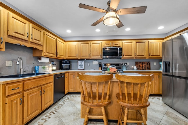 kitchen featuring light countertops, a sink, a ceiling fan, a kitchen island, and appliances with stainless steel finishes