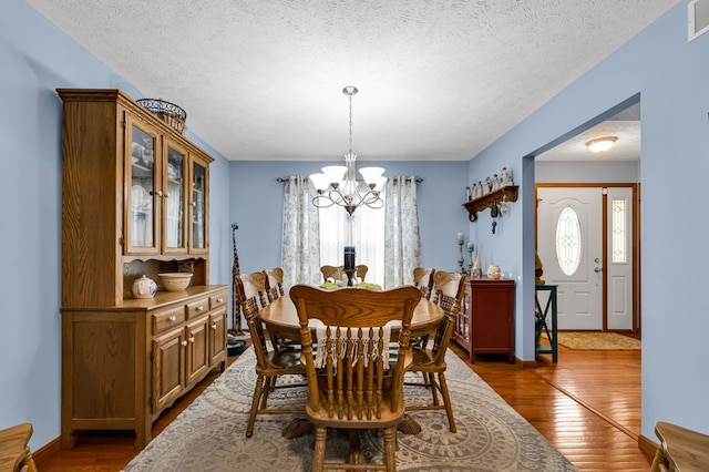 dining area with a textured ceiling, visible vents, baseboards, dark wood finished floors, and an inviting chandelier