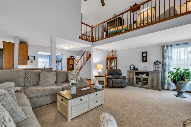 living area featuring stairway, a chandelier, light colored carpet, visible vents, and a towering ceiling