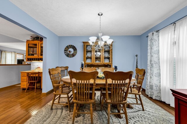 dining space with baseboards, a textured ceiling, wood finished floors, and a notable chandelier
