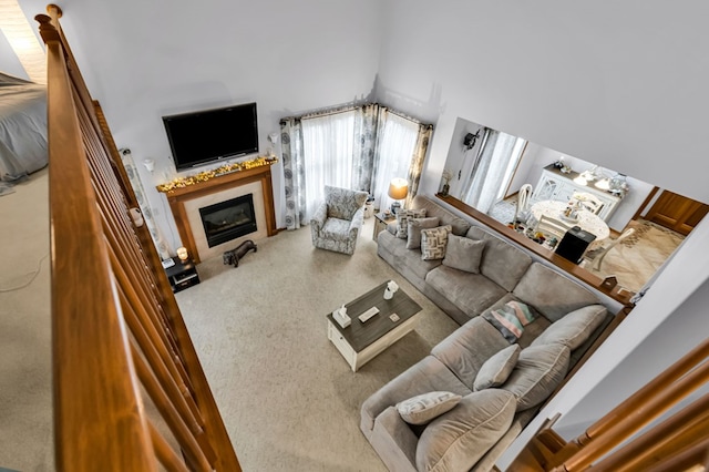living room with carpet, a towering ceiling, and a glass covered fireplace