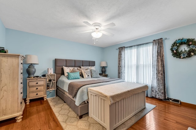 bedroom with a textured ceiling, visible vents, a ceiling fan, and wood finished floors