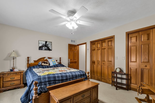 bedroom with light carpet, a textured ceiling, visible vents, and a ceiling fan