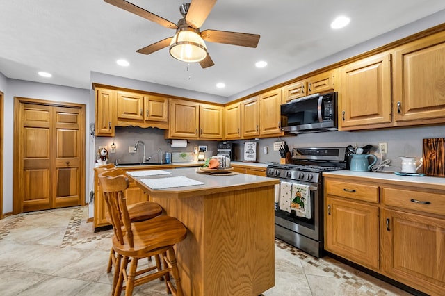 kitchen featuring light countertops, a ceiling fan, appliances with stainless steel finishes, a sink, and a center island