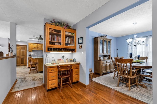 dining area with ceiling fan with notable chandelier, baseboards, light wood-style floors, and a textured ceiling