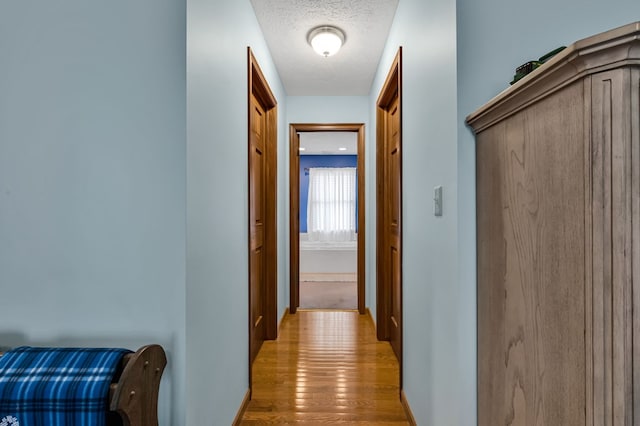 hallway featuring baseboards, a textured ceiling, and light wood-type flooring