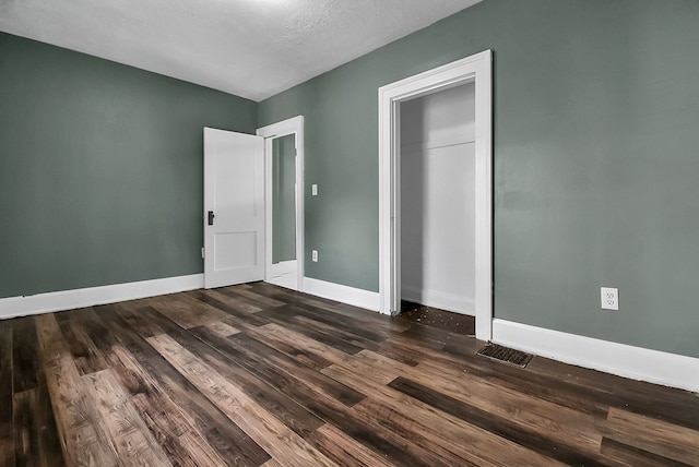 unfurnished bedroom featuring dark wood-type flooring, a closet, visible vents, and baseboards