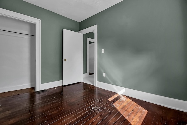 unfurnished bedroom featuring visible vents, a closet, hardwood / wood-style flooring, and baseboards