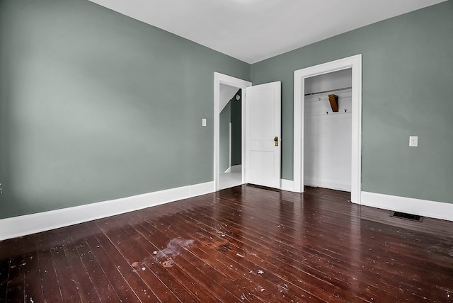 unfurnished bedroom featuring a closet, wood-type flooring, visible vents, and baseboards