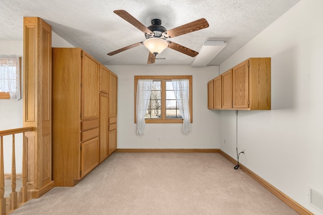 unfurnished bedroom featuring a textured ceiling, visible vents, baseboards, a ceiling fan, and light carpet