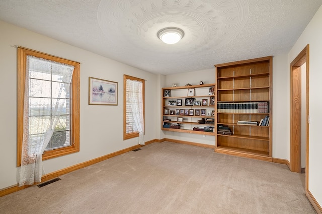 unfurnished room featuring baseboards, visible vents, light colored carpet, and a textured ceiling
