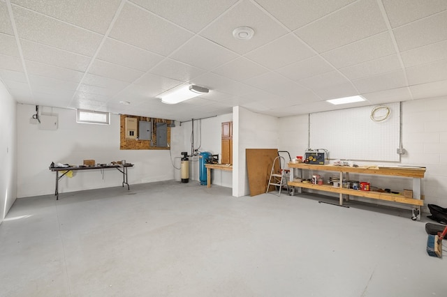 basement featuring concrete block wall, a drop ceiling, electric panel, and a workshop area