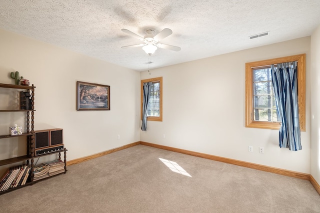 carpeted empty room with baseboards, visible vents, a healthy amount of sunlight, and a ceiling fan