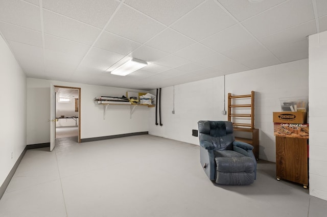 sitting room with concrete block wall, baseboards, and a paneled ceiling