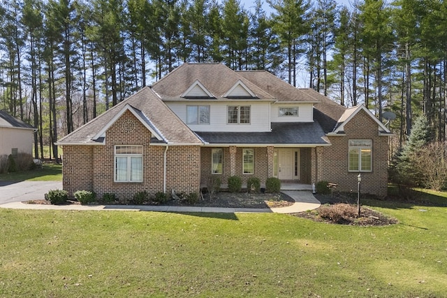 view of front of property with a shingled roof, a front yard, and brick siding