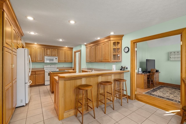 kitchen featuring a kitchen bar, a peninsula, light tile patterned flooring, and white appliances