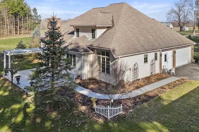 exterior space with driveway, a shingled roof, an attached garage, and a lawn