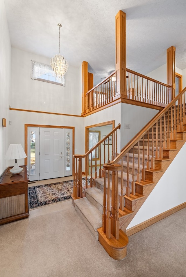 carpeted foyer entrance featuring baseboards, a high ceiling, an inviting chandelier, and stairway
