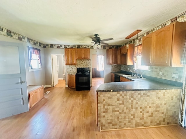 kitchen with kitchen peninsula, sink, black appliances, pendant lighting, and light hardwood / wood-style flooring