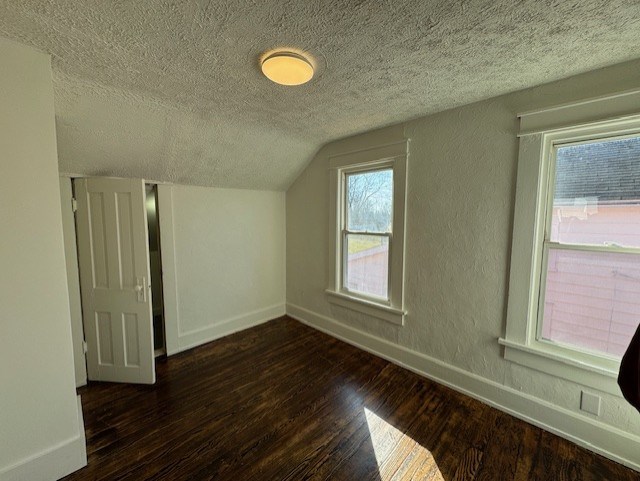 additional living space featuring hardwood / wood-style flooring, a textured ceiling, baseboards, vaulted ceiling, and a textured wall