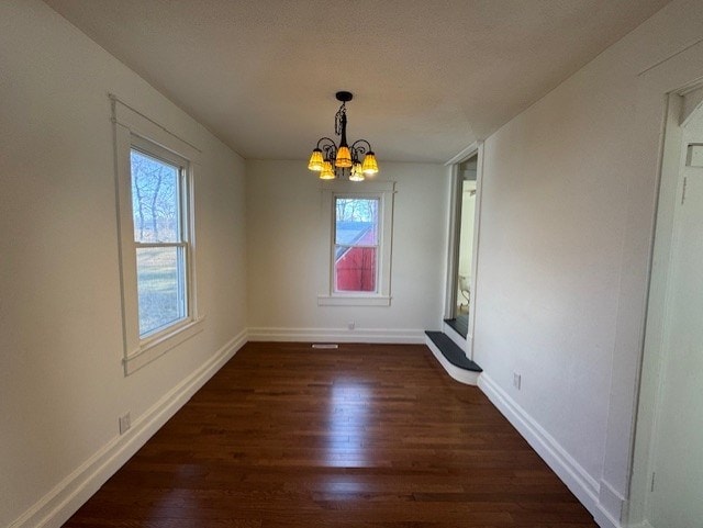 unfurnished dining area with baseboards, dark wood-type flooring, and a chandelier